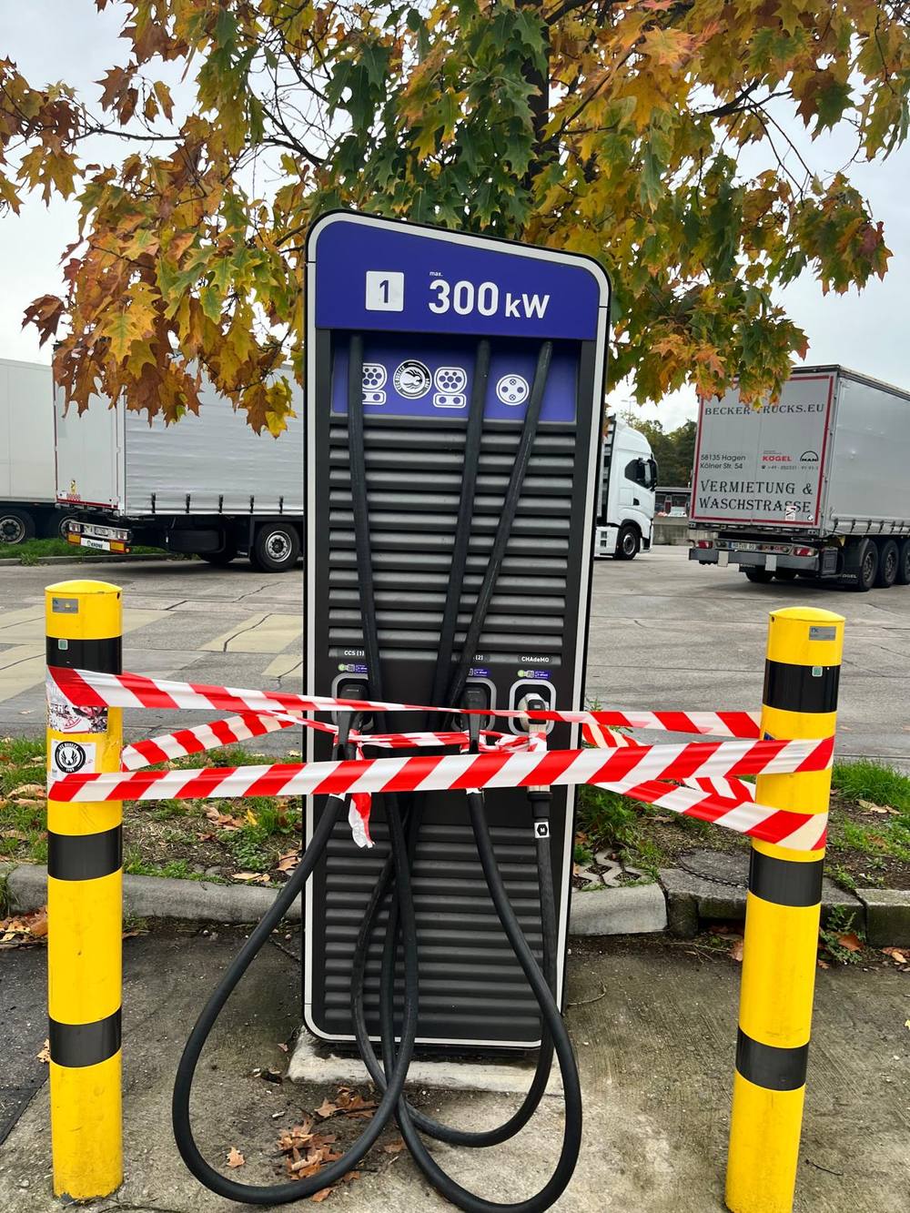 A 300 kW public fast charger cordoned off with red and white hazard tape between two yellow bollards at a highway rest stop